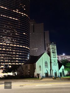 Kościół w centrum Houston nocą na tle drapaczy chmur Downtown, kontrast historycznej architektury i nowoczesnych wieżowców. 